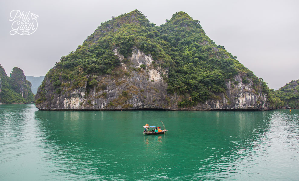 A lone boat next to a towering karst island