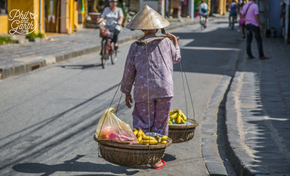 Fruit vendor carrying a traditional yoke with baskets full of bananas